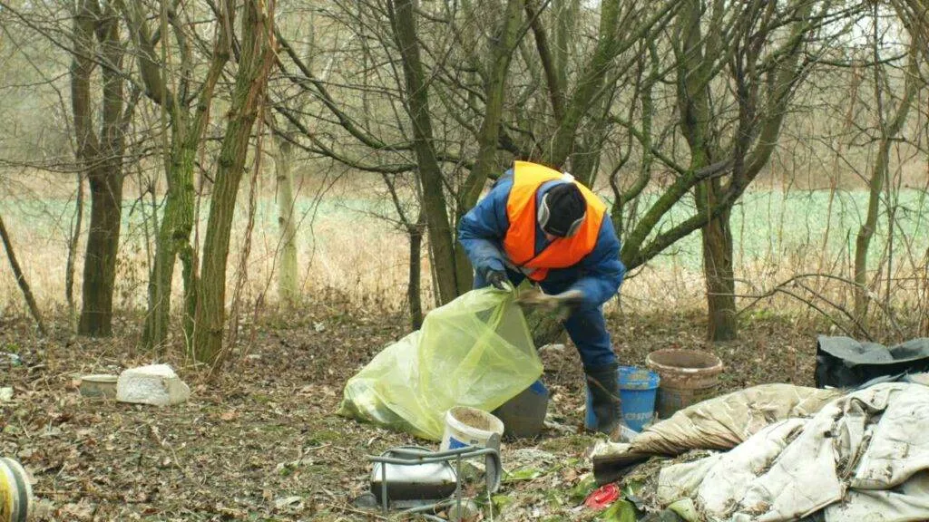 OLOMOUC, CZECH REPUBLIC, JANUARY 2, 2019: Man collect garbage rubbish gathers bag, forest landscape in endangered nature, black dump of human dirt of plastic trash various kinds
